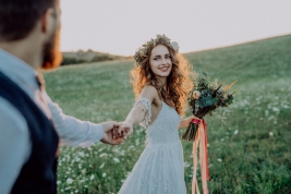 Beautiful young bride and groom outside in green nature at romantic sunset, holding hands.