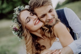 Beautiful young couple, groom and bride with flower wreath outside in green nature.