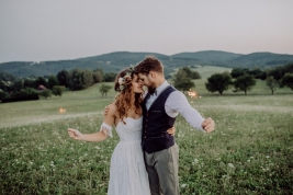 Beautiful young bride and groom with sparklers hugging outside in green nature.