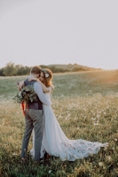 Beautiful young bride and groom hugging outside in green nature at romantic sunset.